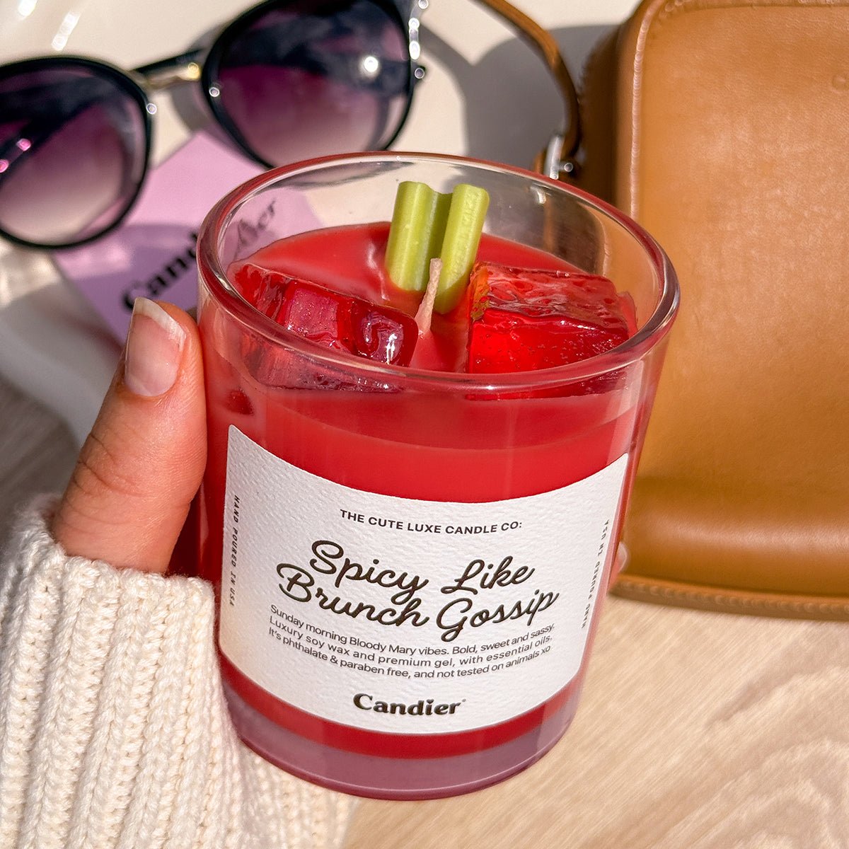Hand holding Candier tomato candle with Bloody Mary scent and celery garnish, ideal for tomato girl brunch decor.