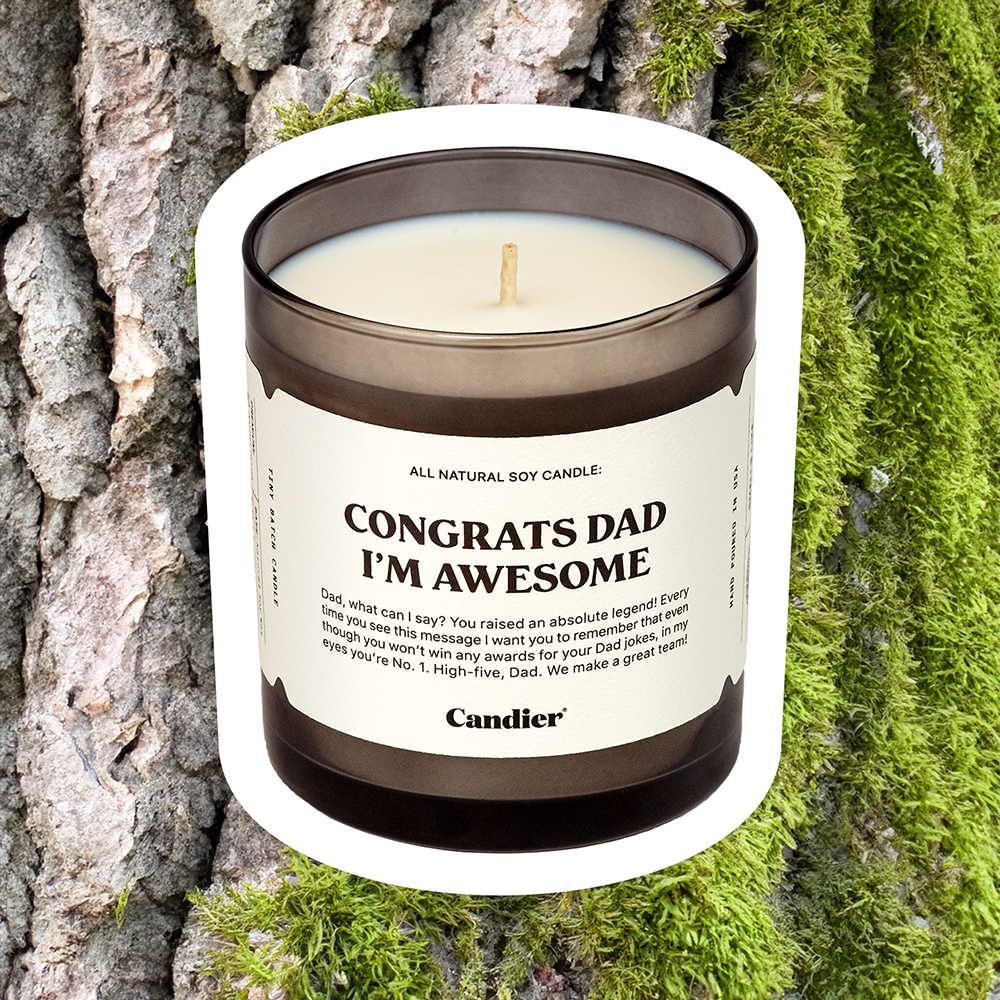 a manly looking candle with a label that reads Congrats Dad I'm awesome, with tree bark and moss in the background 
