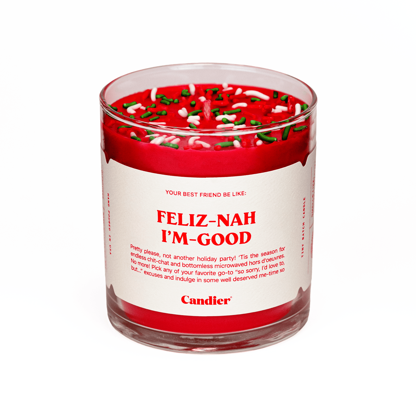 A Candier candle in a clear glass vessel, filled with Santa red wax, topped with red, green and white sprinkles, and a white label that reads “Feliz Nah I’m Good”