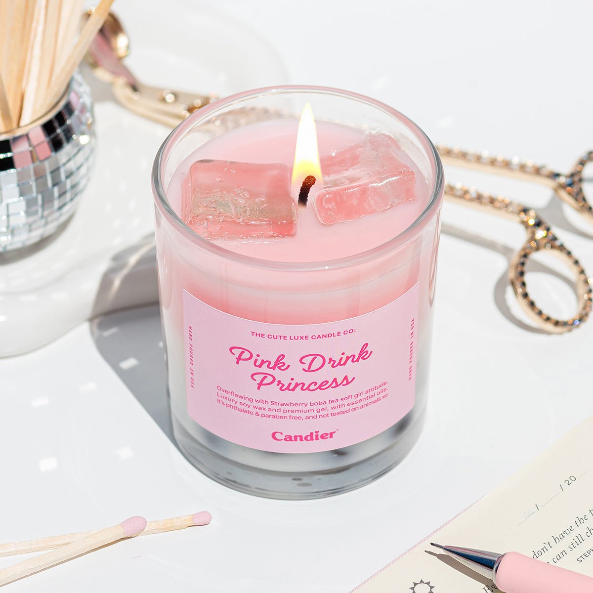 Pink strawberry candle labeled 'Pink Drink Princess' with a lit wick with soft girl era aesthetic