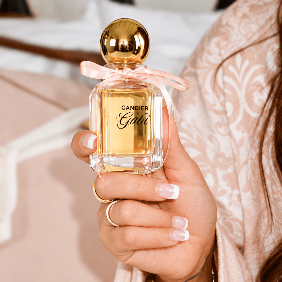 Hand holding Candier x Gabi Pink Air perfume with the front logo, pink ribbon and gold cap visible.