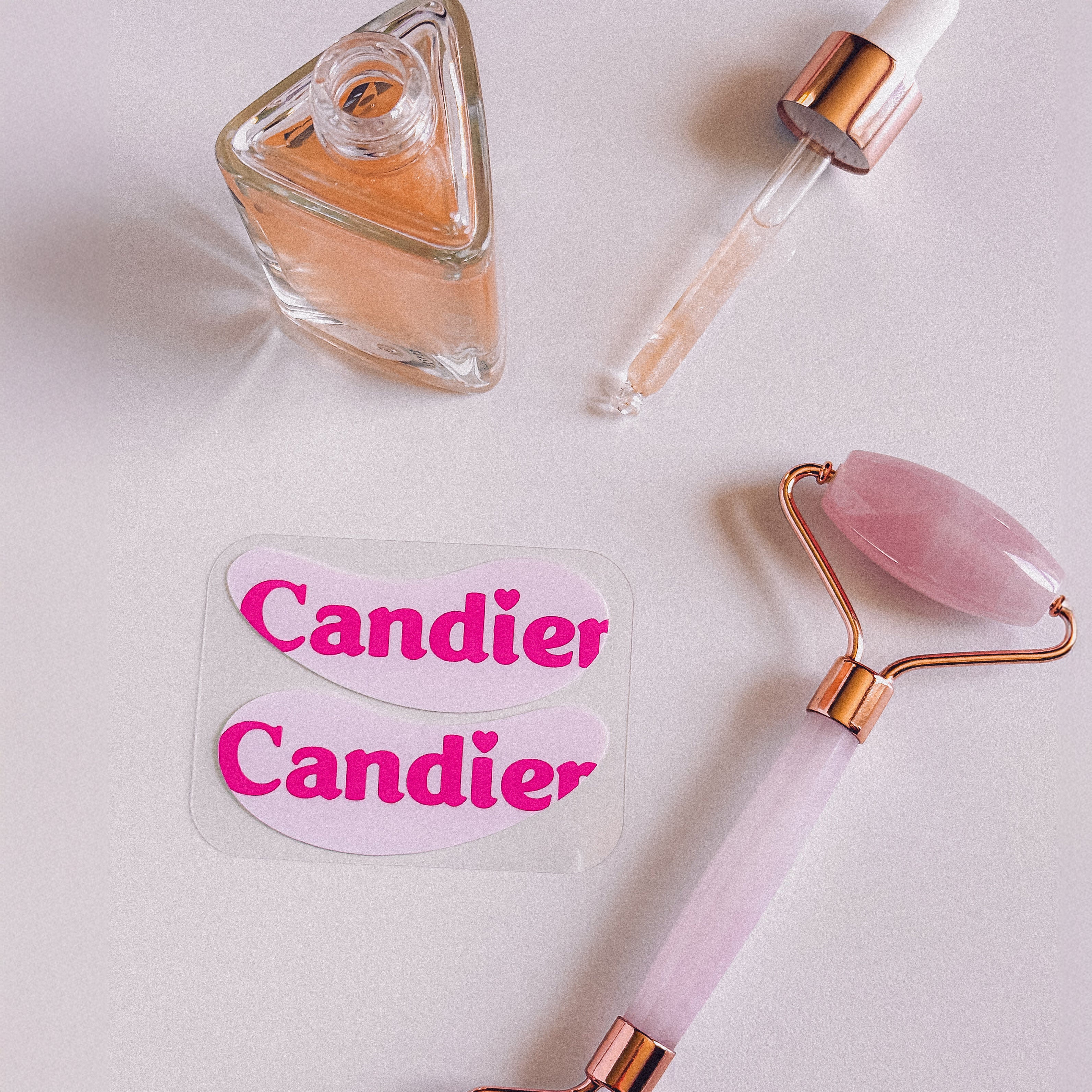 Reusable Candier under eye patches with bold logo design, styled with serum dropper and pink jade roller – cute reusable eye mask for skincare gift