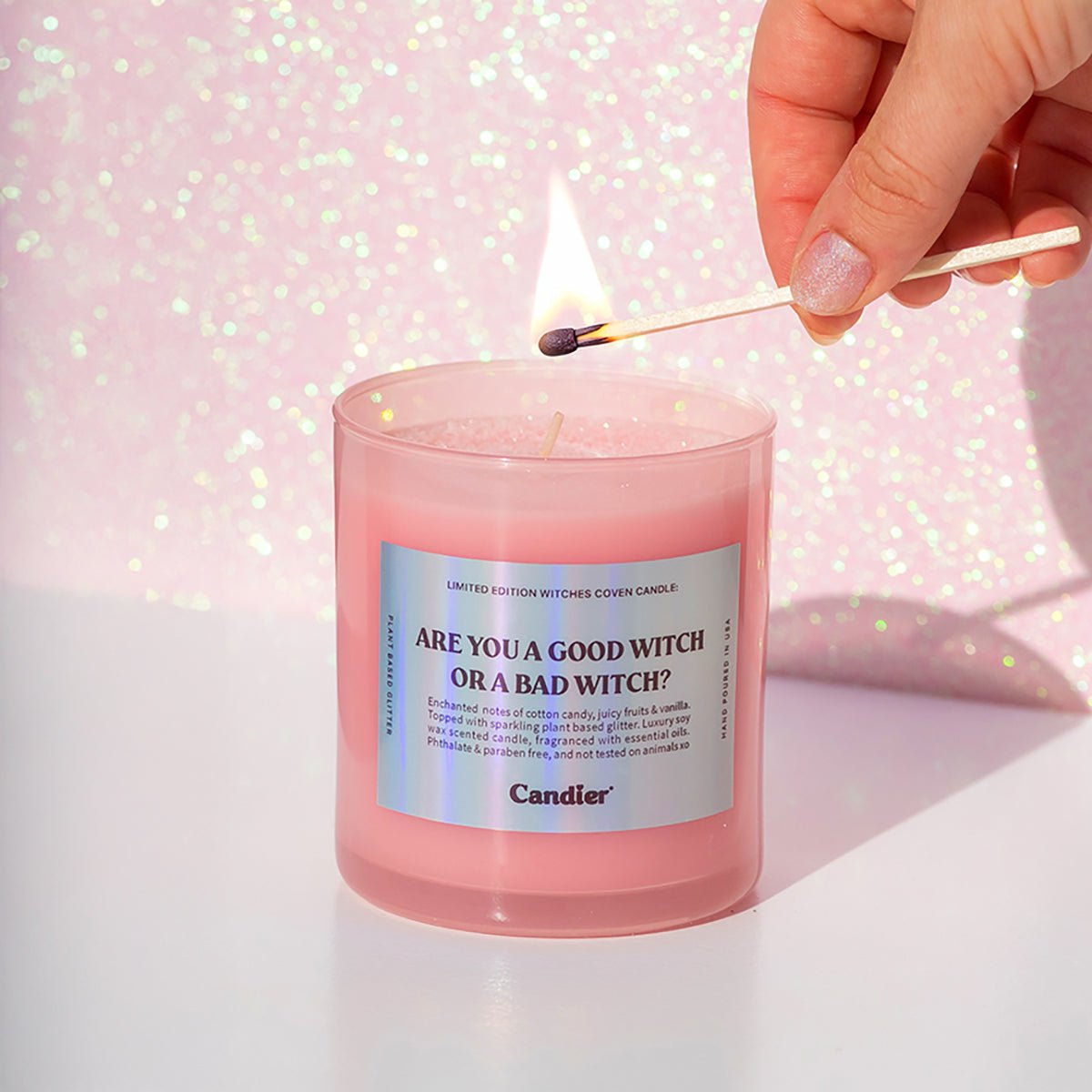 A hand lighting the CandierĀ® Are You a Good Witch or a Bad Witch candle, showing sparkly wax and a cozy vibe, one of the best gifts for teen girls and cute candle lovers.