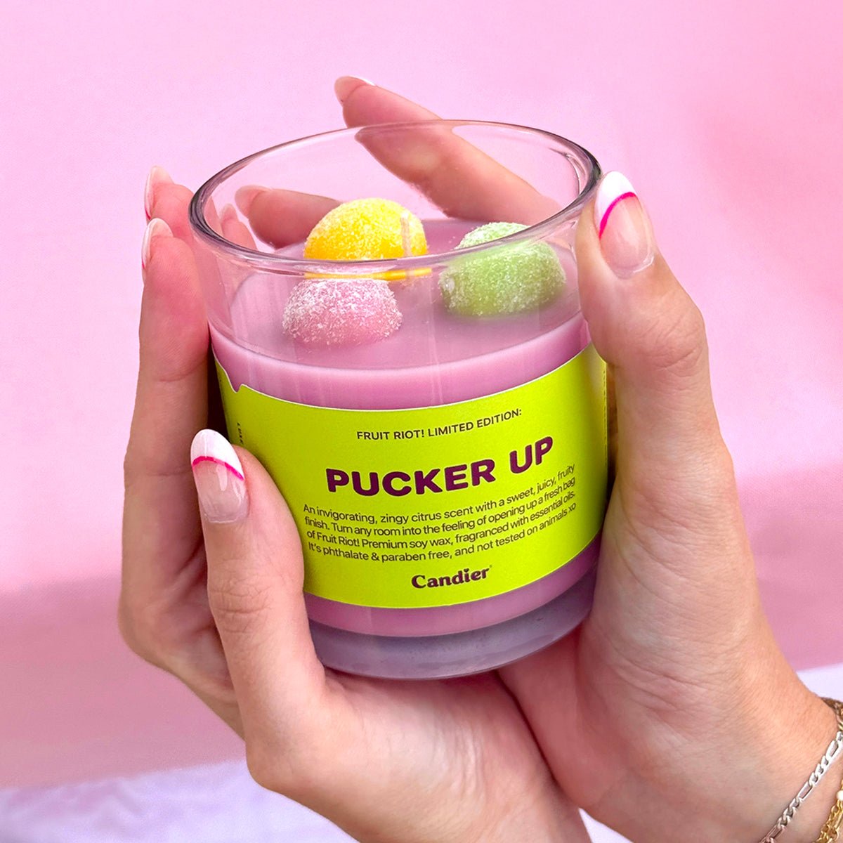 Hand holding Candier Fruit Riot Sour Grapes candle, a pink aesthetic citrus candle with candycore details. A fun, nostalgic food-scented candle from one of the best candle brands in NYC.