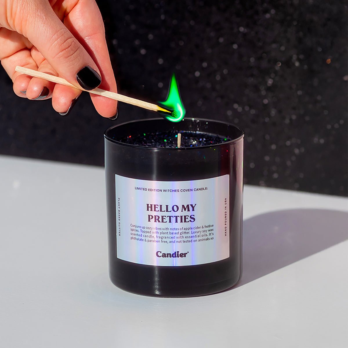 A hand lighting the CandierĀ® Hello My Pretties candle, showing sparkly black wax and bold wicked energy ā a luxe Halloween candle for moody aesthetic lovers.