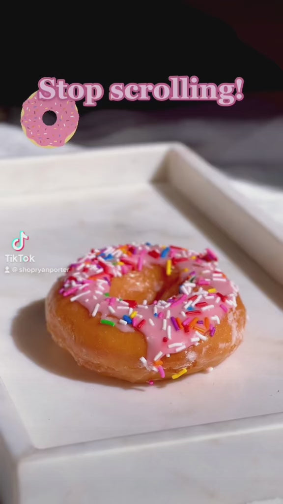 A creative candle designed to look like a glazed donut with pink icing and colorful sprinkles on top.