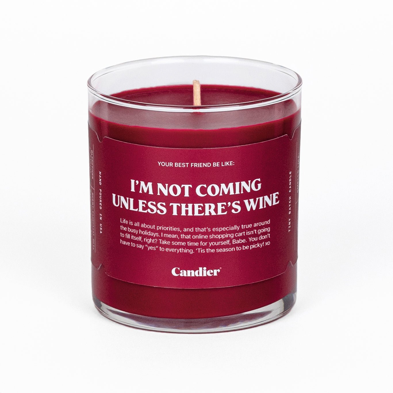 A Candier candle in a glass vessel filled with festive red wax and a label that reads "I'm not coming unless there's wine"