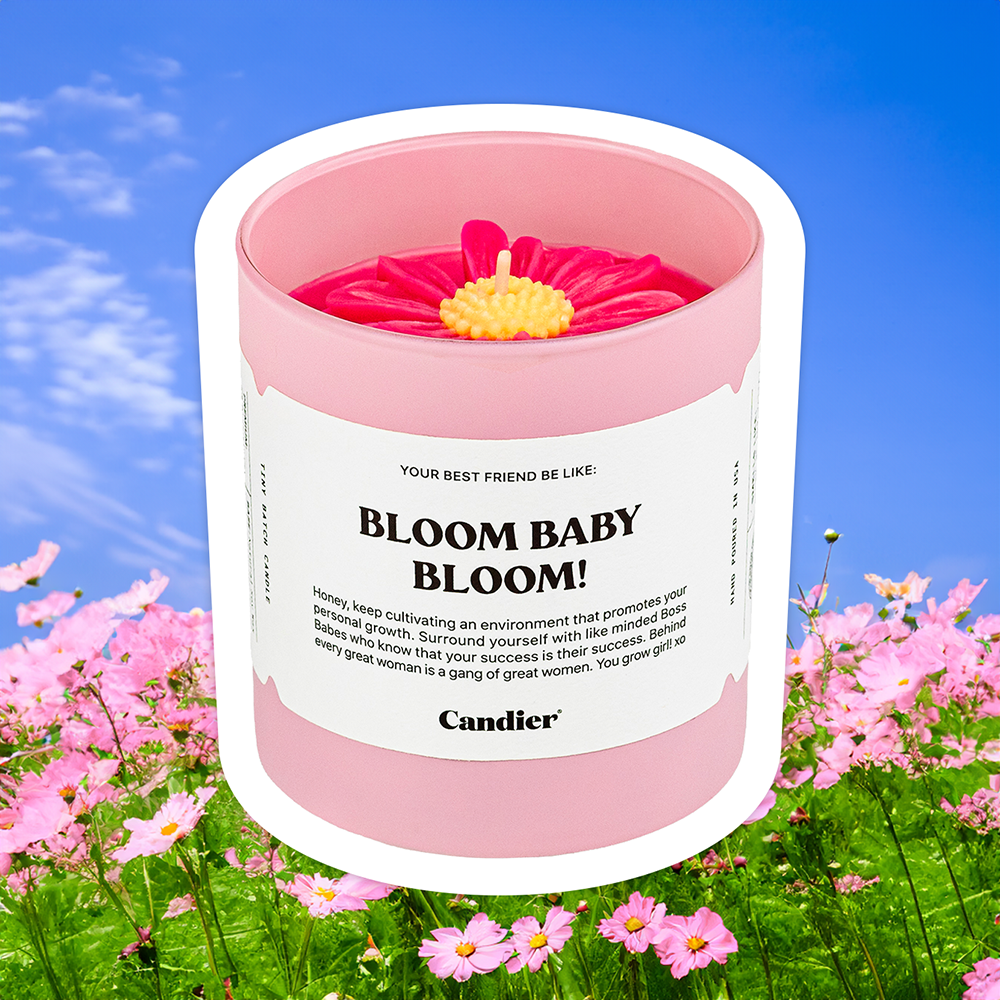 a cute pink candle with a large molded wax flower , shown on a background of a field and blue sky,  and a label that reads Bloom Baby Bloom