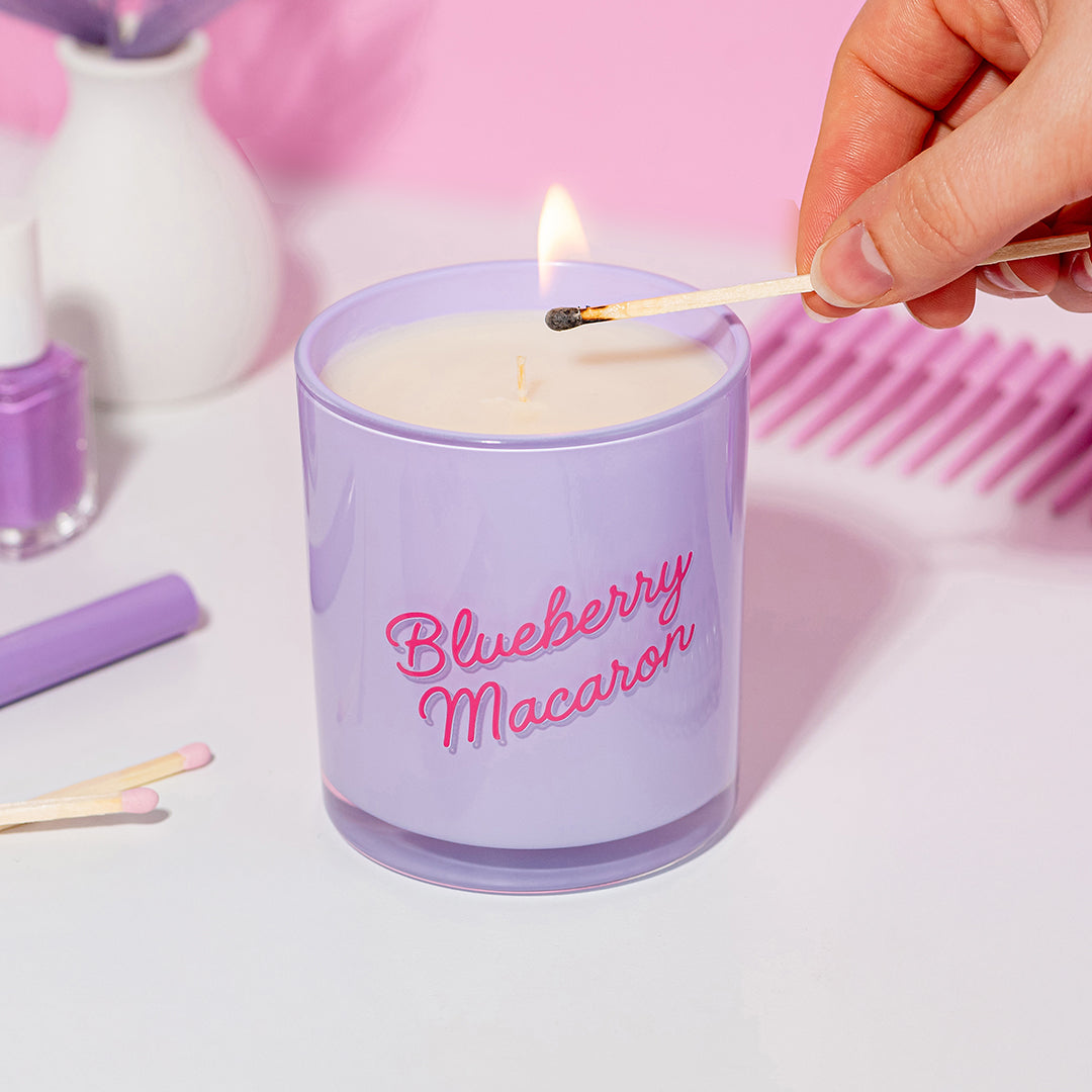 Hand lighting the Candier Blueberry Macaron candle on a pink and purple dresser. Features soft girl aesthetic, gourmand scent and vanilla fragrance