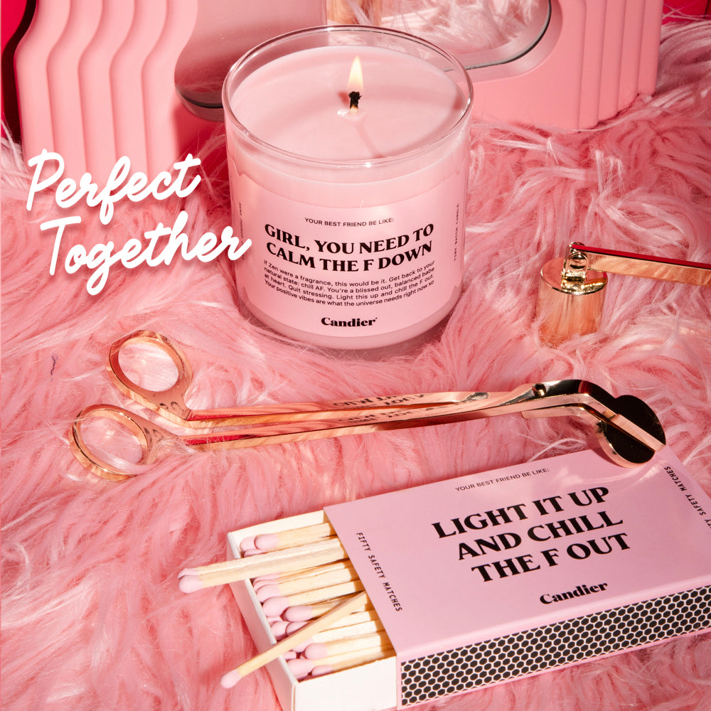 a cute pink candle with a label that reads Girl you need to calm the F down, surrounded buy a gold wick trimmer and a candle flame snuffer