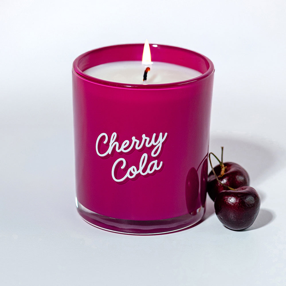 Candier Cherry Cola candle shown with fresh cherries. Aesthetic food-inspired soy wax candle featuring notes cherry vanilla fragrance​, cola, and vanilla scent.