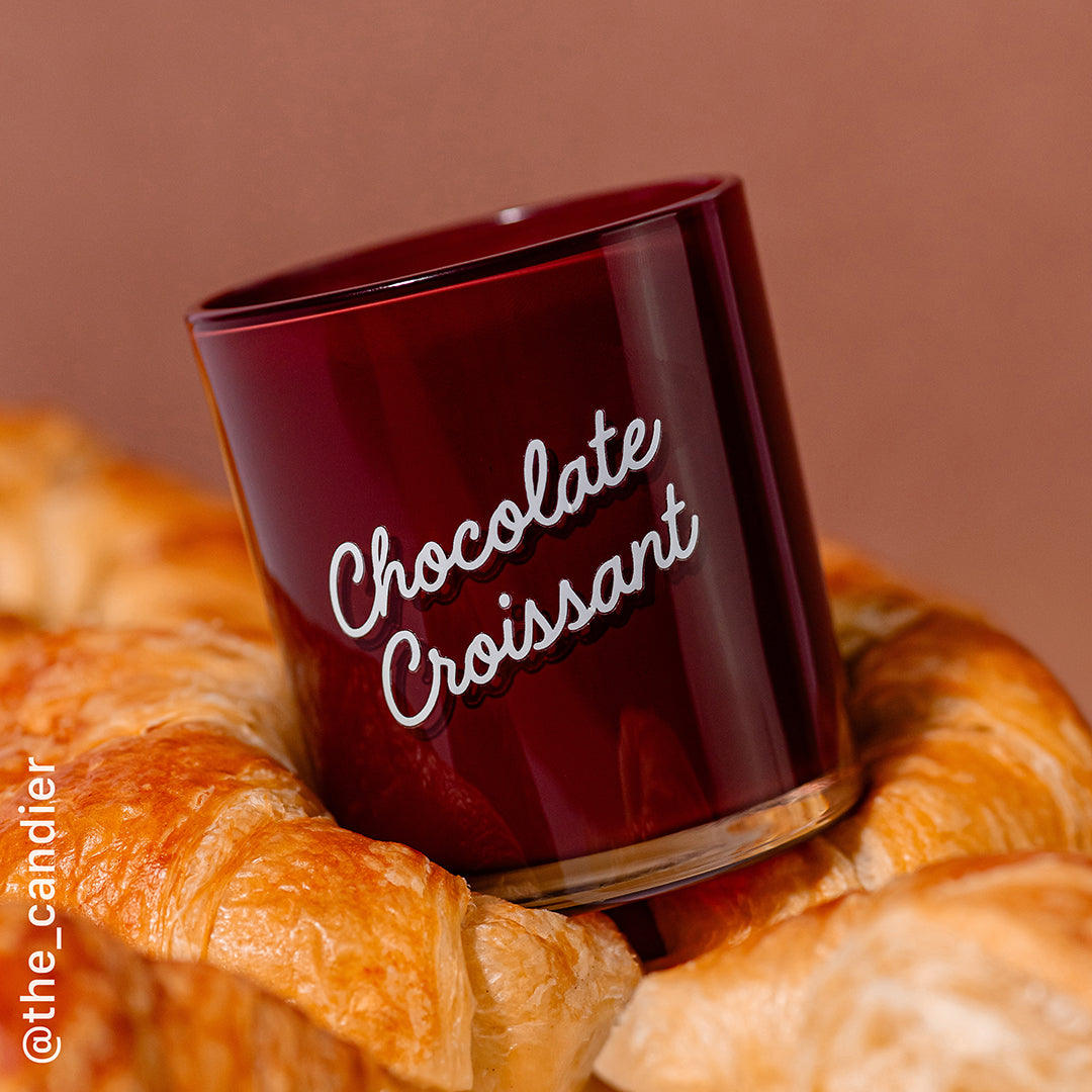 Side angle of Candier Chocolate Croissant candle surrounded by golden croissants. Aesthetic food candle for dessert candle collectors and cute gift givers.