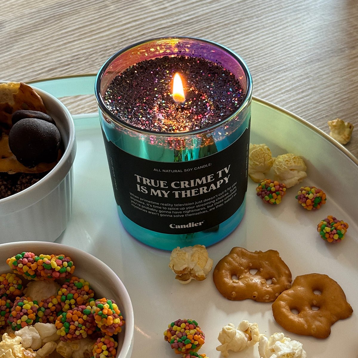 CAndier Candle labeled 'True Crime TV is my Therapy' on a table with halloween snacks