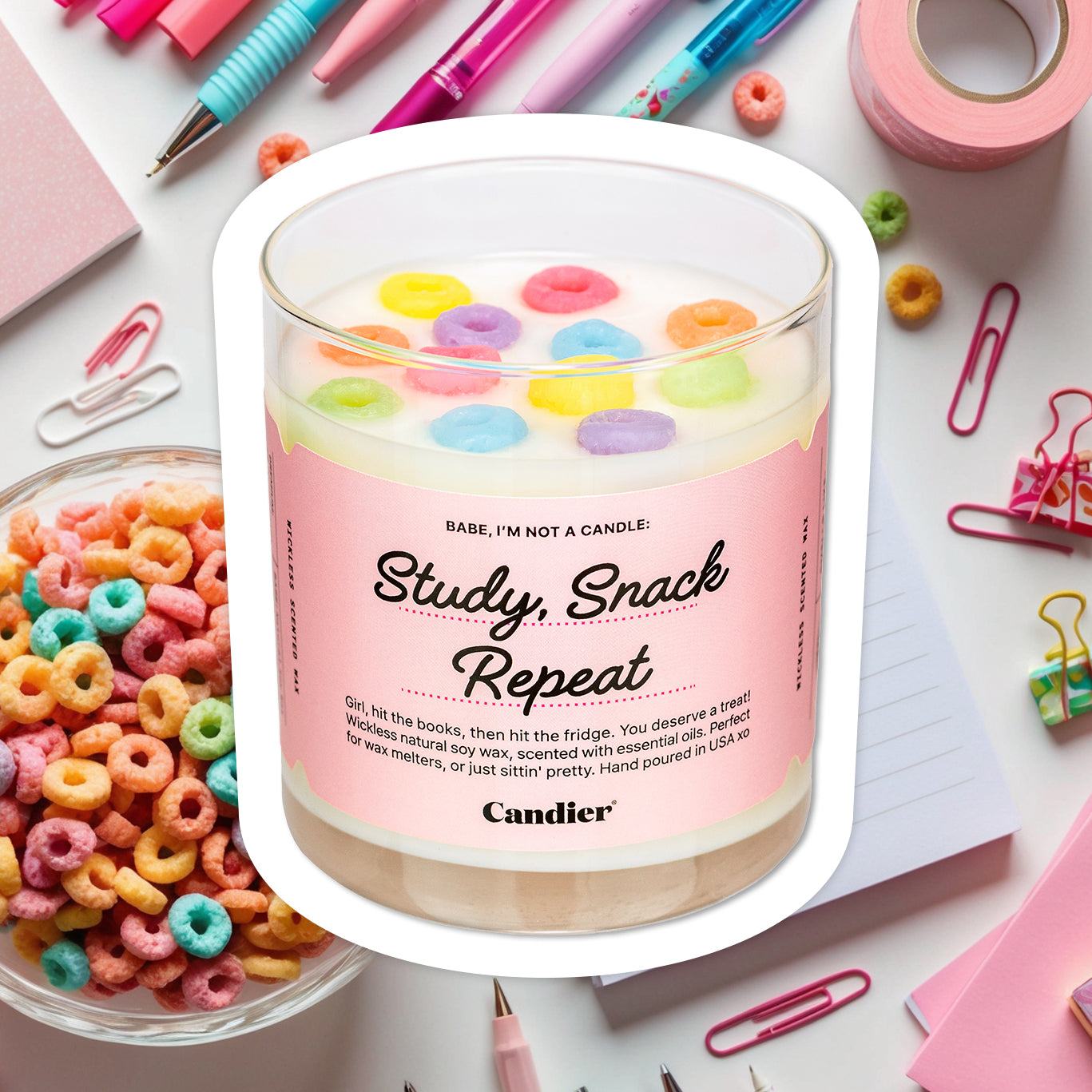 A wickless candle wax melt topped with colorful wax fruit loop cereal, and alabel that reads Study, Snack, Repeat by CANDIER, with a background of a cute desk with a cereal bowl and girly stationary