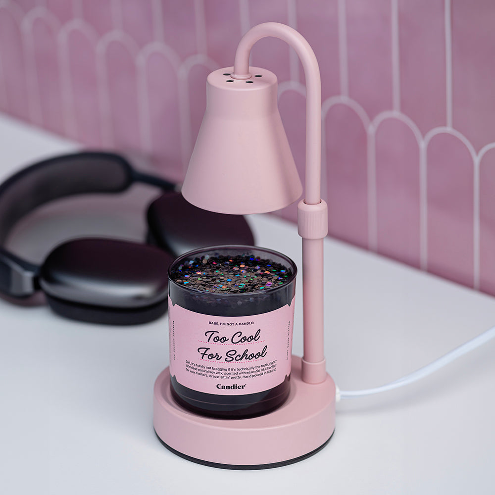 a glossy black wickless candle wax melt with a pink label that reads Too Cool For School. Dormables by CANDIER, sitting on a pink lamp style wax melter