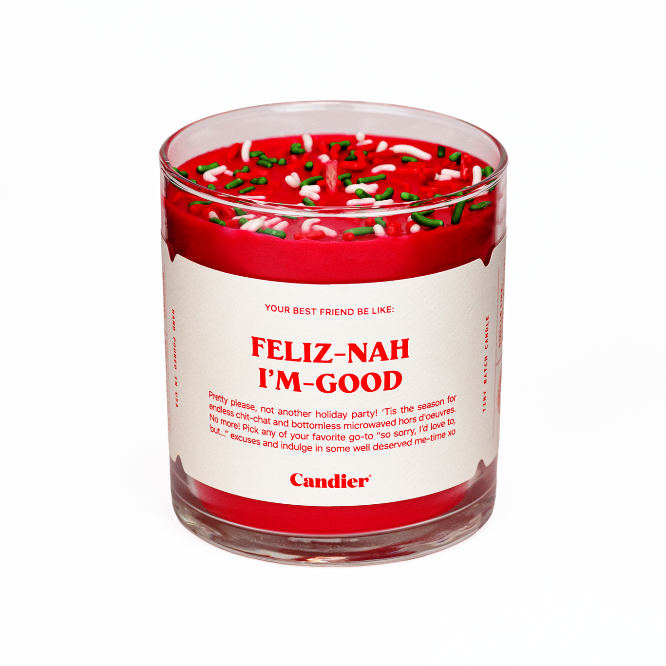 A Candier candle in a clear glass vessel, filled with Santa red wax, topped with red, green and white sprinkles, and a white label that reads “Feliz Nah I’m Good”