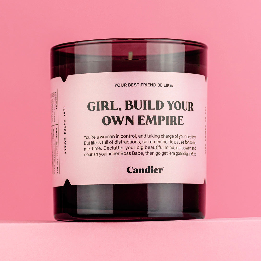 A black glass candle with a pink label that reads Girl Build Your Own Empire