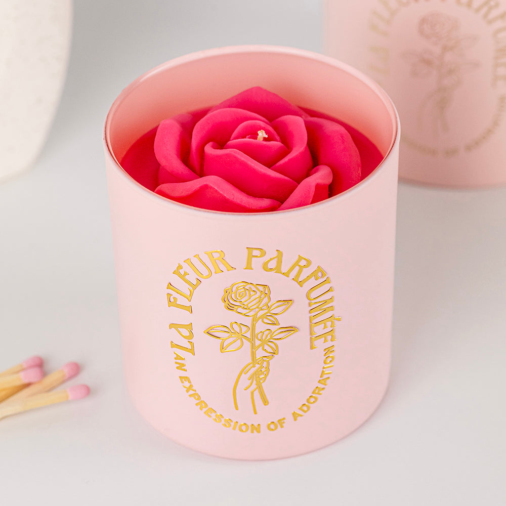 An elegant luxurious light pink candle with a gold emblem that reads La Fleur Parfumée An Expression of Adoration, and is topped with a hot pink sculpted wax rose