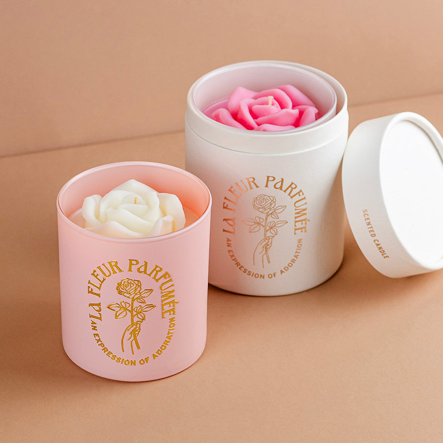 A pair of luxury, high end candles topped with sculpted wax roses . One candle is in a premium gift box