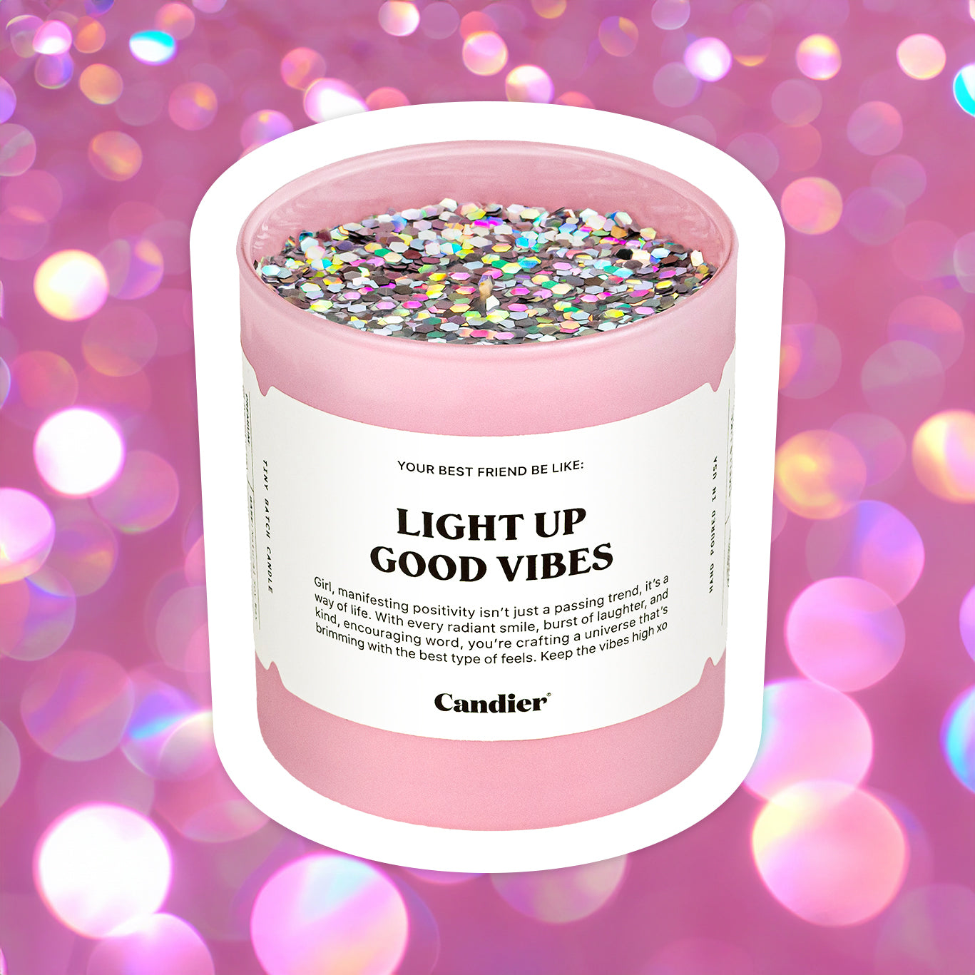 A pink candle with sparkling holographic glitter on top and a label that reads light up good vibes