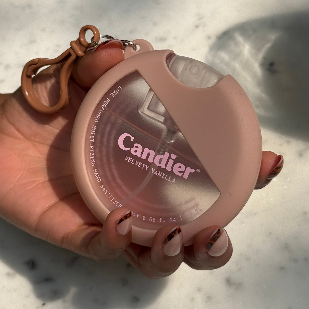 Hand holding Candier moisturizing scented hand sanitizer​ spray with vanilla scent and gourmand fragrance, with cute holder keychain