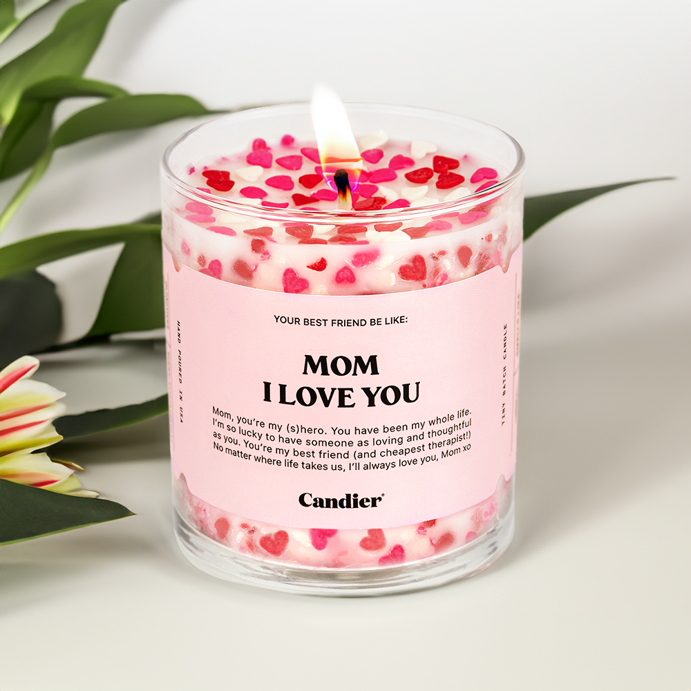 A candle with red and pink hearts, a label that reads Mom I Love You and flowers in the background
