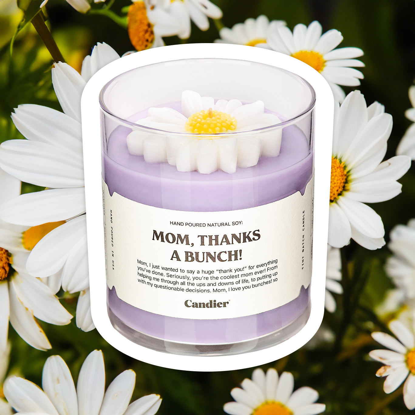 A purple candle with a sculpted wax flower on top and a label that reads Mom Thanks A Bunch. Field of daisies in the background