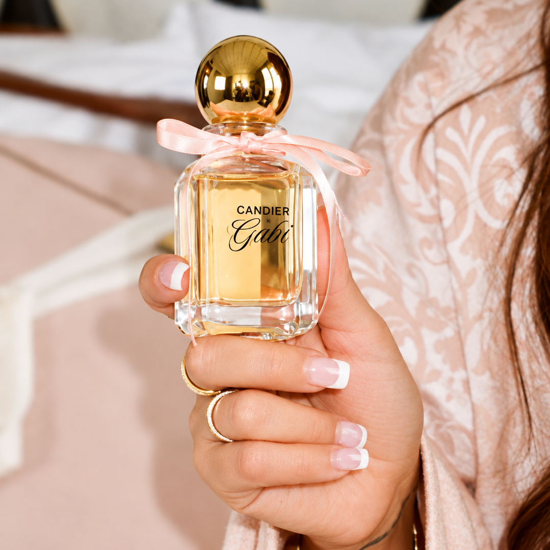 Hand holding Candier x Gabi Pink Air perfume with the front logo, pink ribbon and gold cap visible.