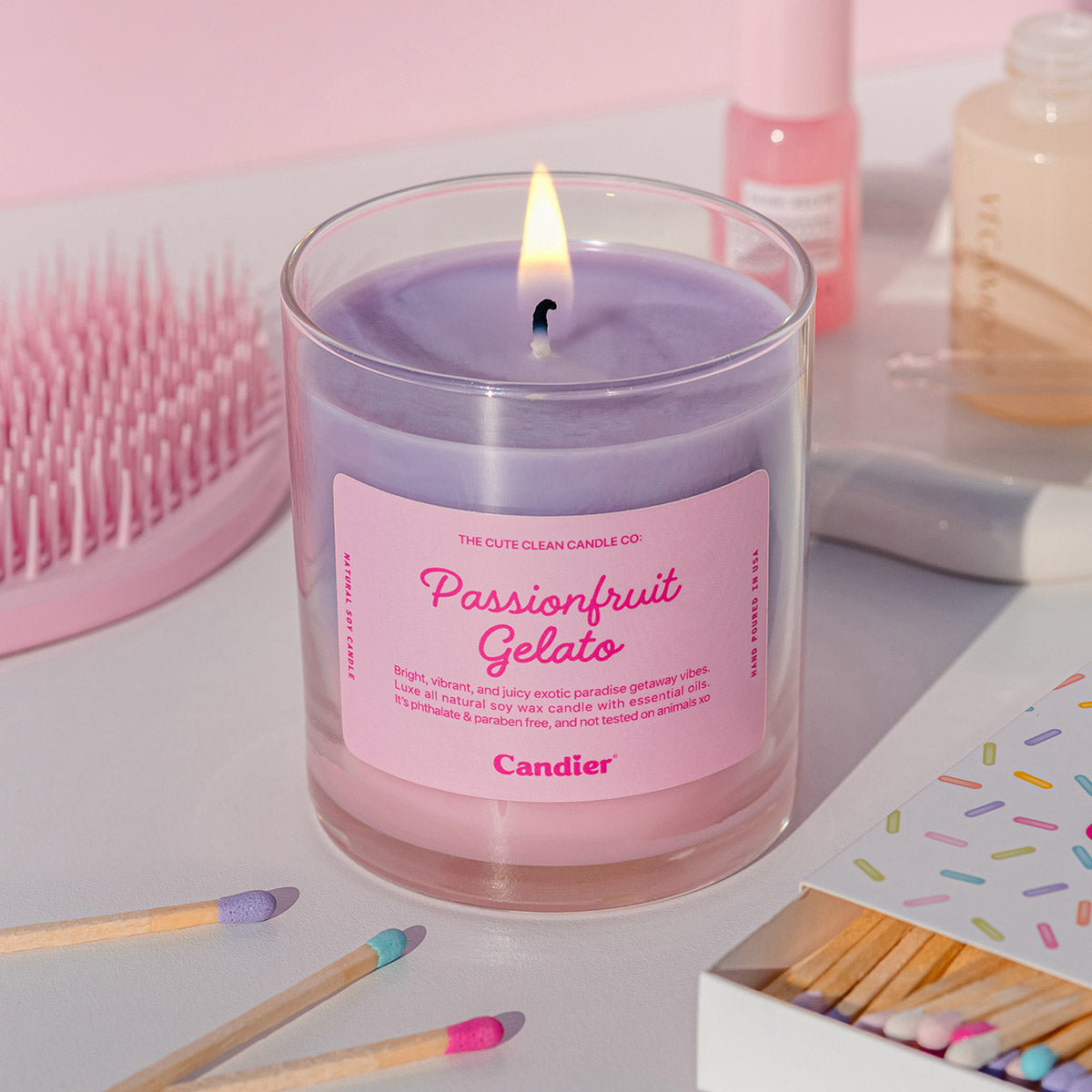Hand lighting the Candier Passionfruit Gelato Candle on a vanity with pink accessories—clean girl aesthetic and luxury soy wax.