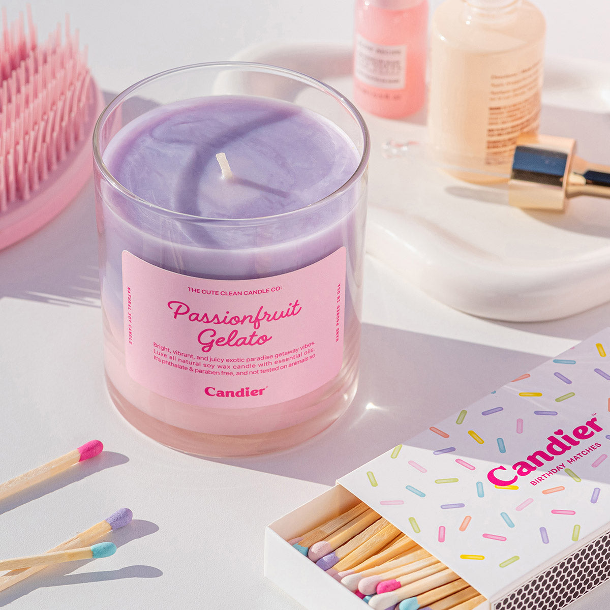 Candier Passionfruit Gelato Candle with aesthetic pink and purple ombre soy wax, styled with pastel matchsticks and luxury beauty products. Soft girl era candle scene with summer vacation vibes.