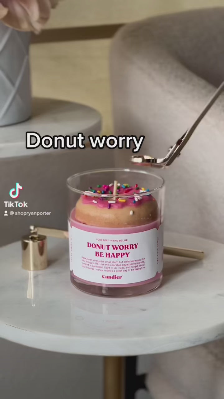 A creative donut-shaped candle with pink frosting and colorful sprinkles, labeled "Donut Worry Be Happy."